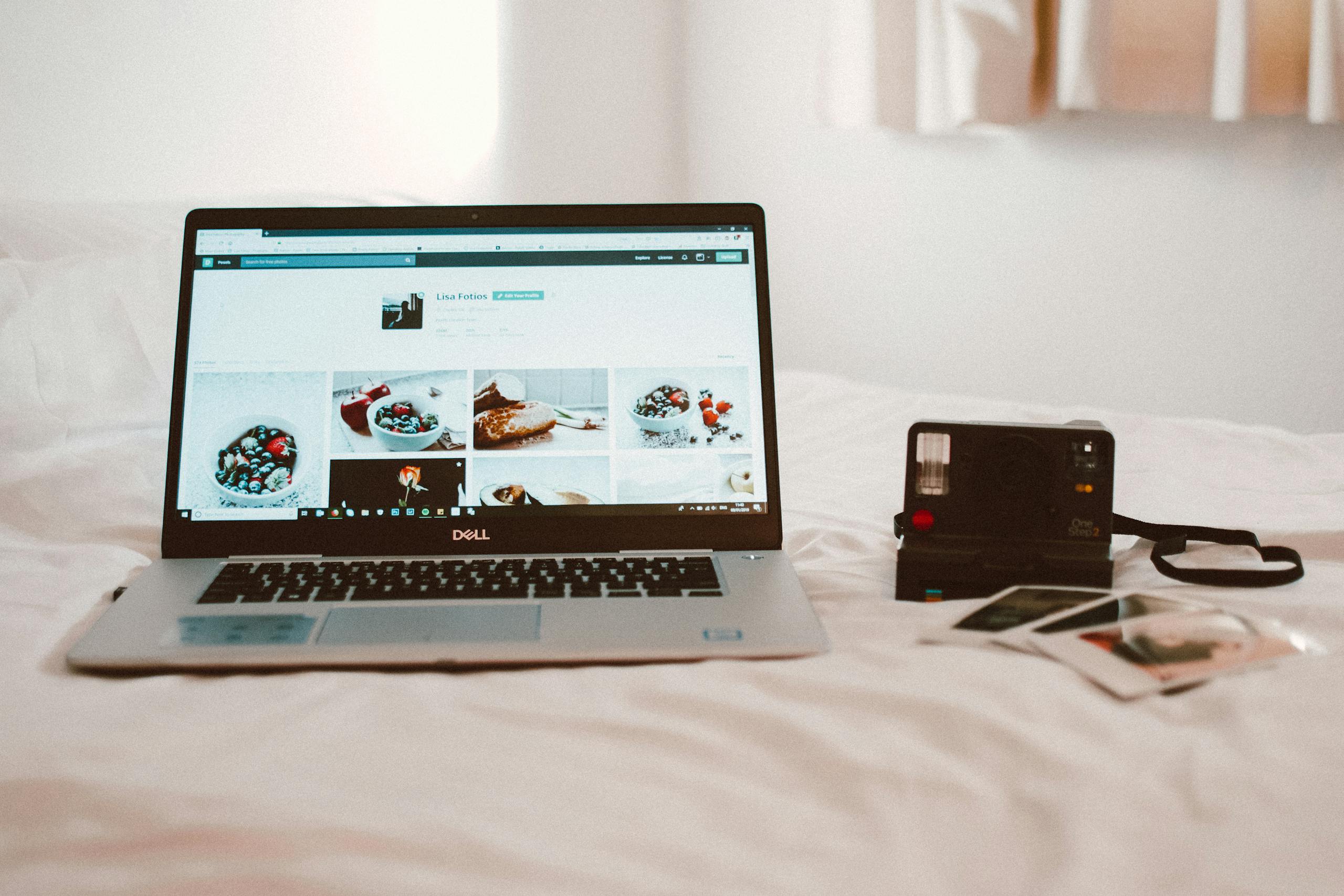 A Dell laptop and vintage camera on a bed create a cozy work environment.