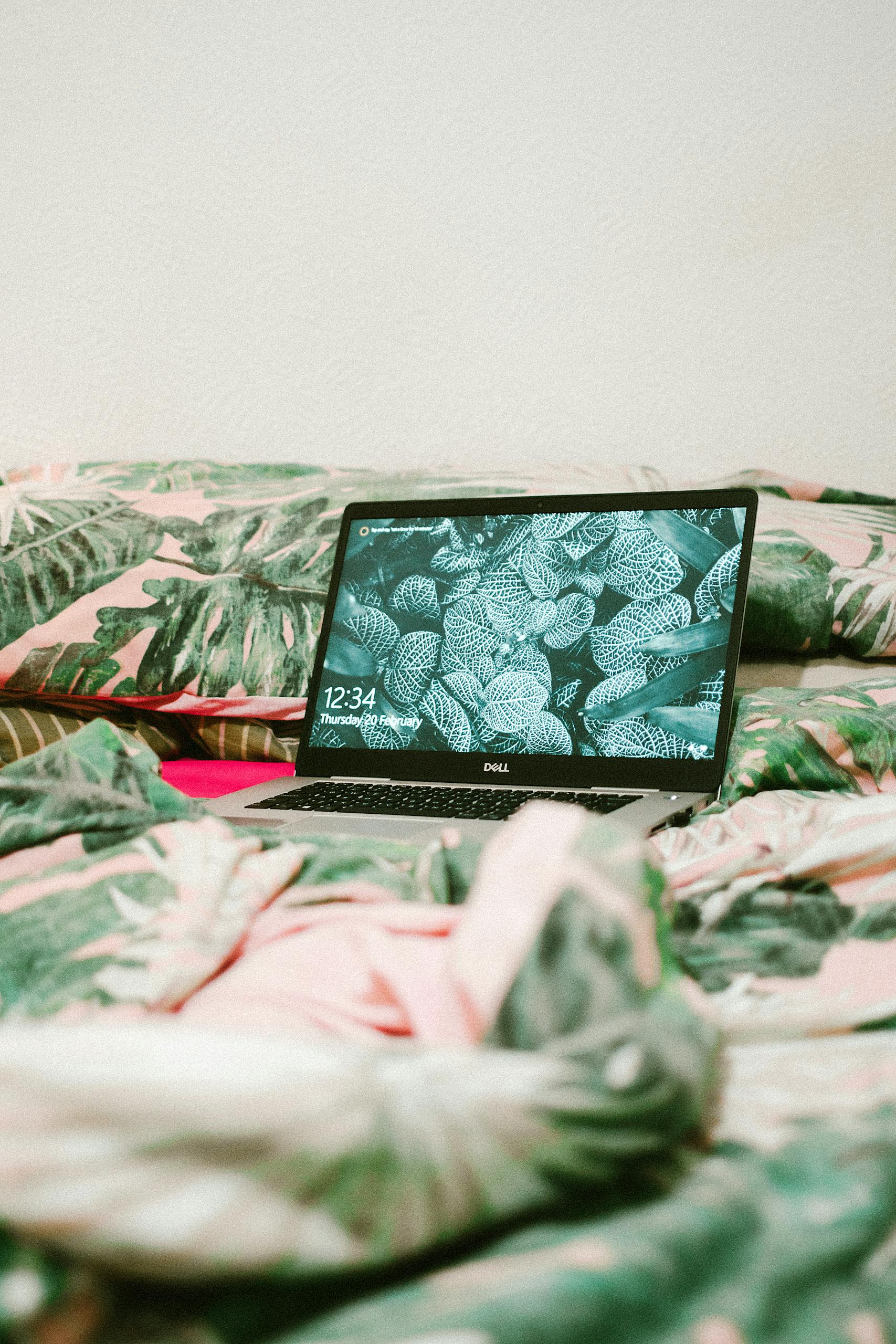 A laptop sits on a bed with tropical leaf print sheets, ideal for remote work and relaxation.